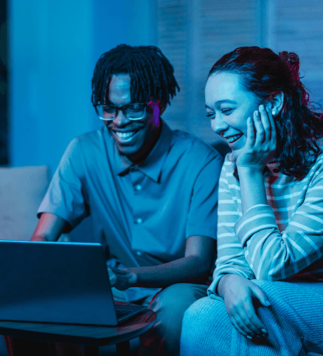 Two people smiling while using a laptop computer.